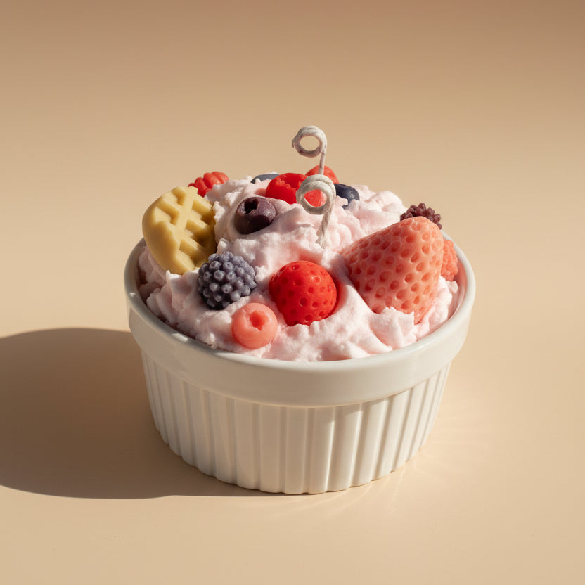 White cup filled with pink whipped cream, berries, and cookies candle on a white background