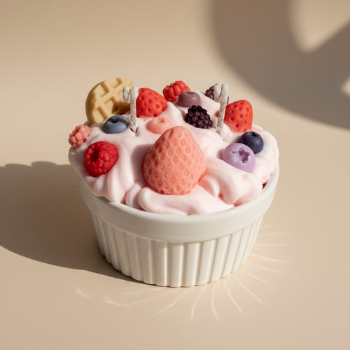 White cup filled with pink whipped cream, berries, and cookies candle on a white background