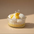 A candle that looks like a dessert in a glass bowl with whipped cream and lemon slices on a beige background