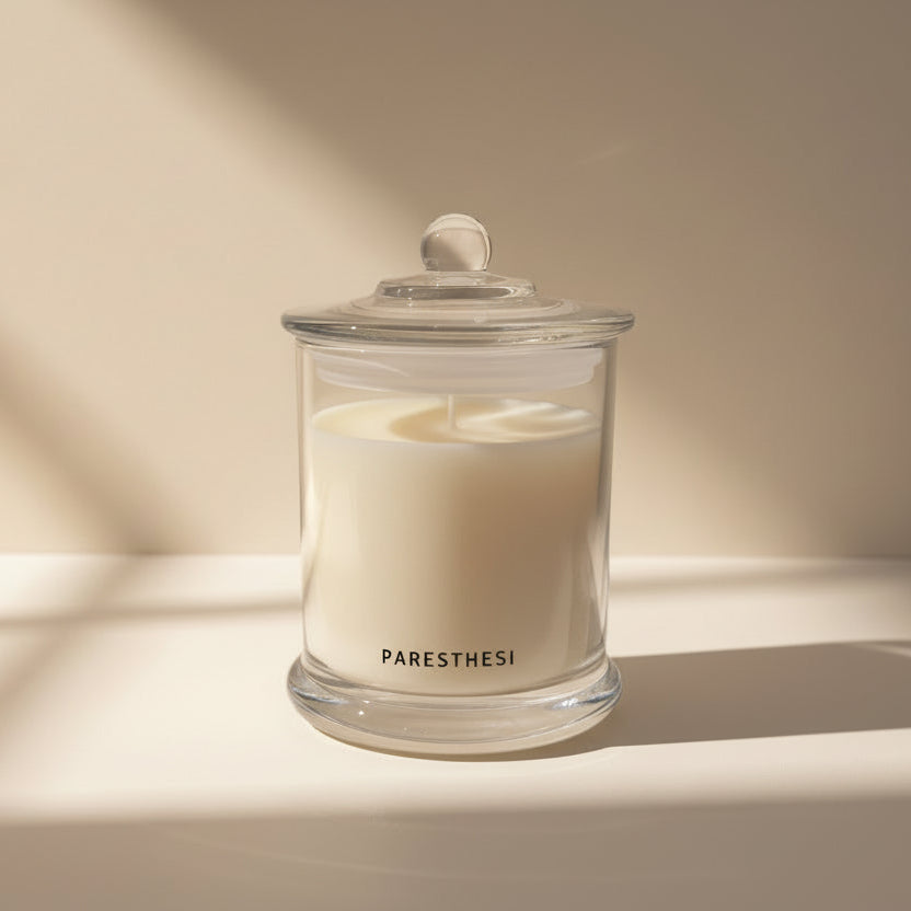 Candle in a glass jar with 'PARESTHESI' branding on a neutral background