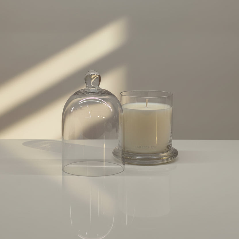 Glass candle holder with a lit candle on a reflective surface with a soft shadow.