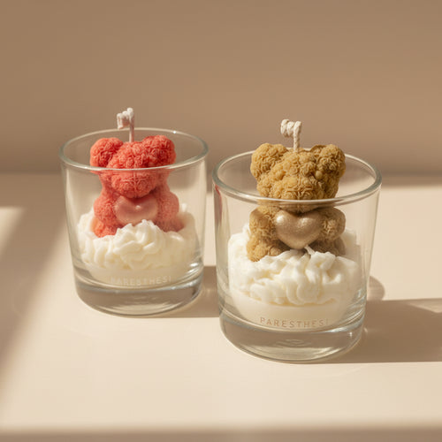 Two glass containers with teddy bear-shaped candles on a neutral background