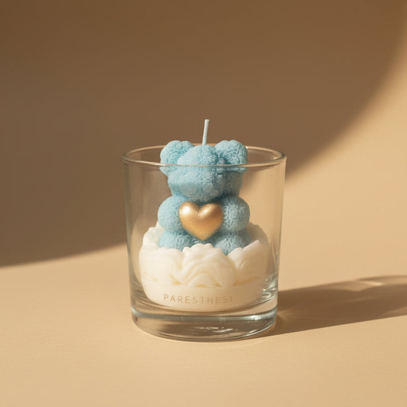 Blue teddy bear-shaped candle in a glass container on a beige background