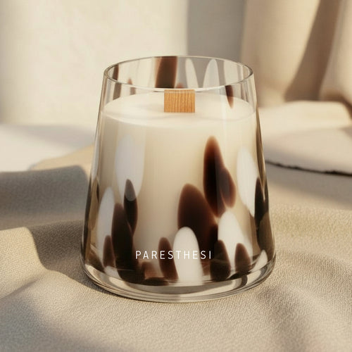 Candle in a glass container with a tortoiseshell pattern on a beige surface, featuring the brand 'PARESTHESI'.