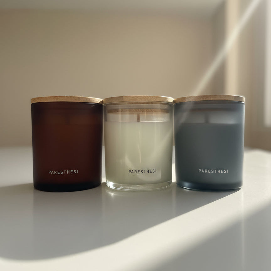Three candles from the brand 'Paresthesi' on a light surface with a neutral background