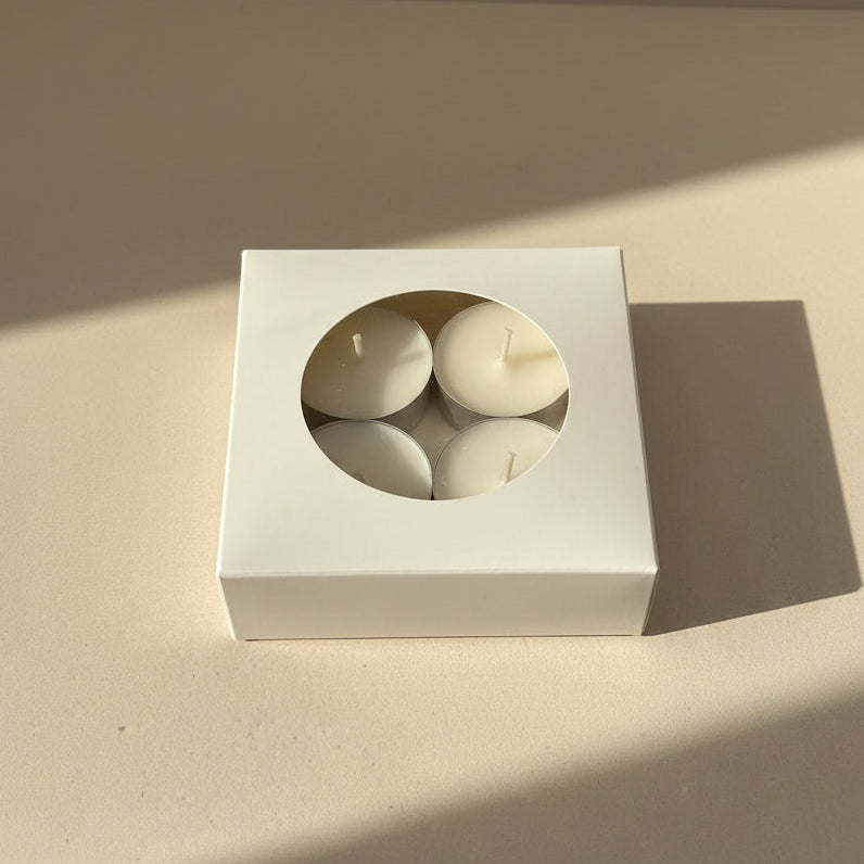 Four white tealight candles in a white box on a light beige background