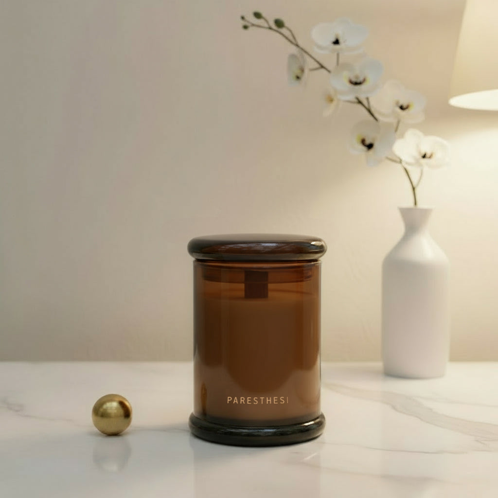 Brown candle with 'PARESTHESI' branding on a white surface with a blurred background