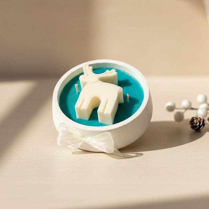 Decorative candle with a white deer figure on a dark green circular base, placed on a light beige surface.