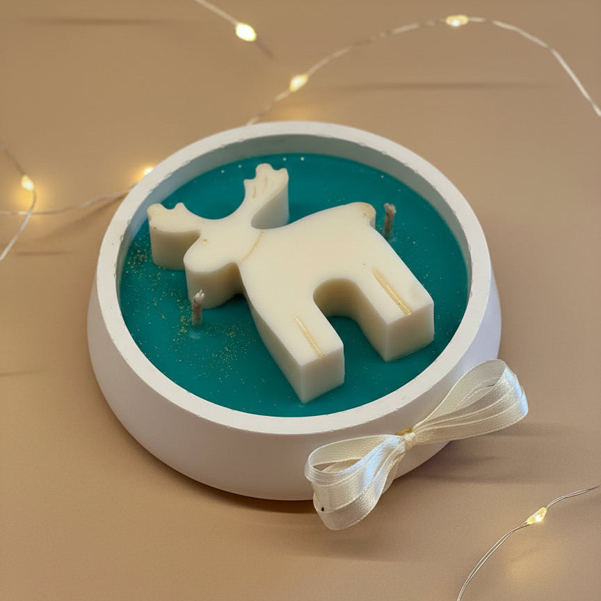 Candle shaped like a reindeer on a teal base with a white ribbon on a beige surface.