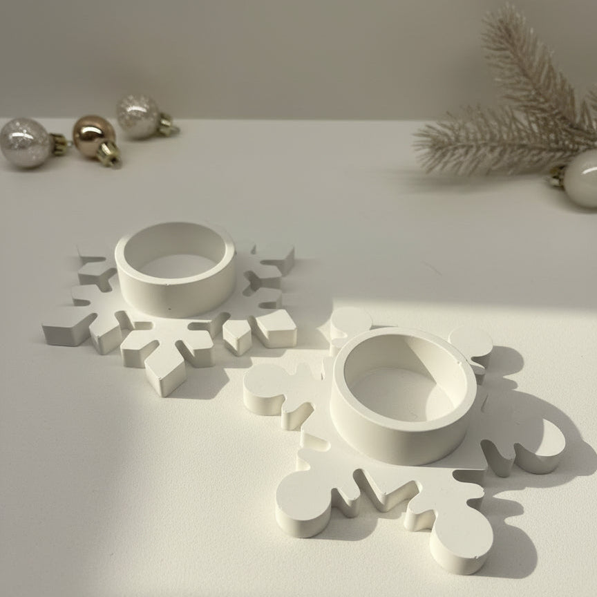 Two white snowflake-shaped candle holders on a beige surface with white and gold ornaments.