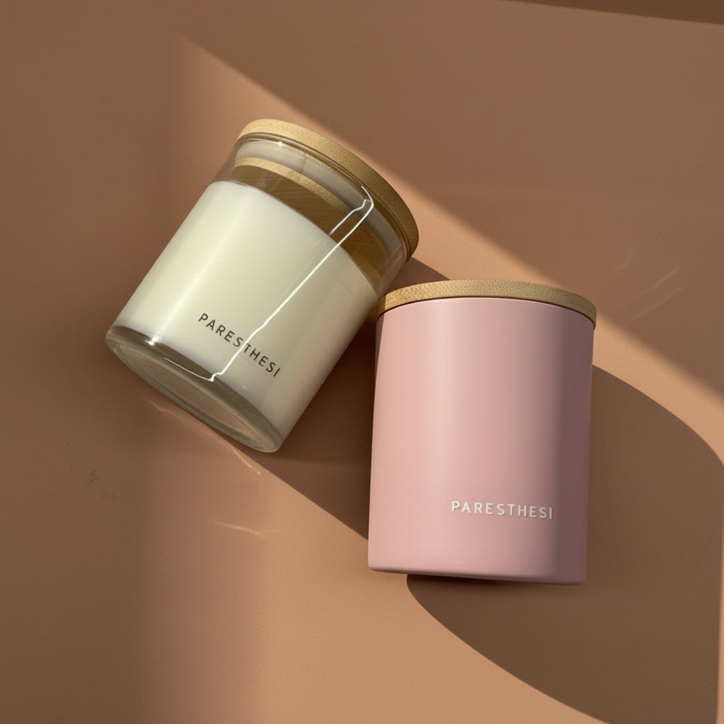 Two candles, one white and one pink, with wooden lids on a brown background. Brand 'PARESTHESI' is visible.