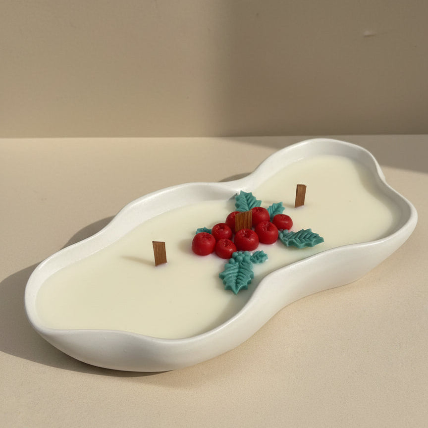Decorative candle with red berries and green leaves on a beige surface