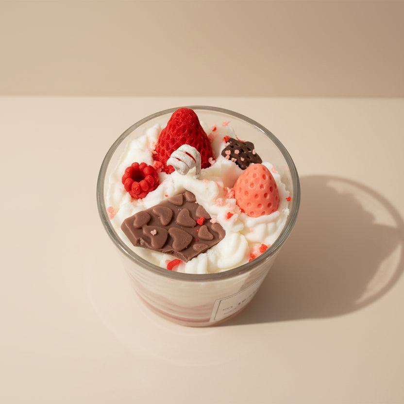 Decorative candle with strawberry, berries, chocolate, and whipped cream design on a white background