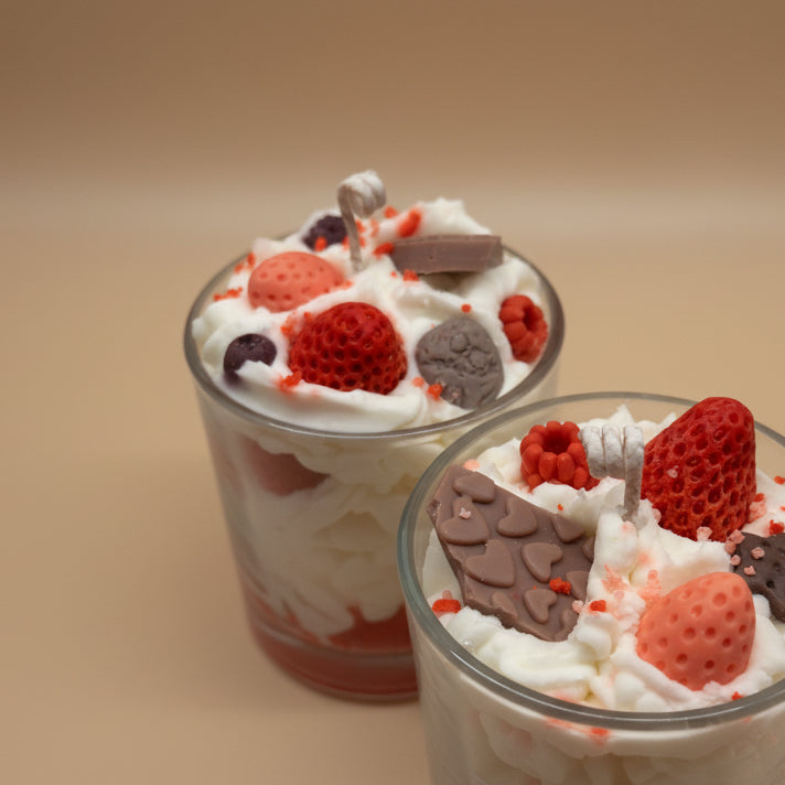 Decorative candle with strawberry, berries, chocolates, syrup, and whipped cream design on a white background