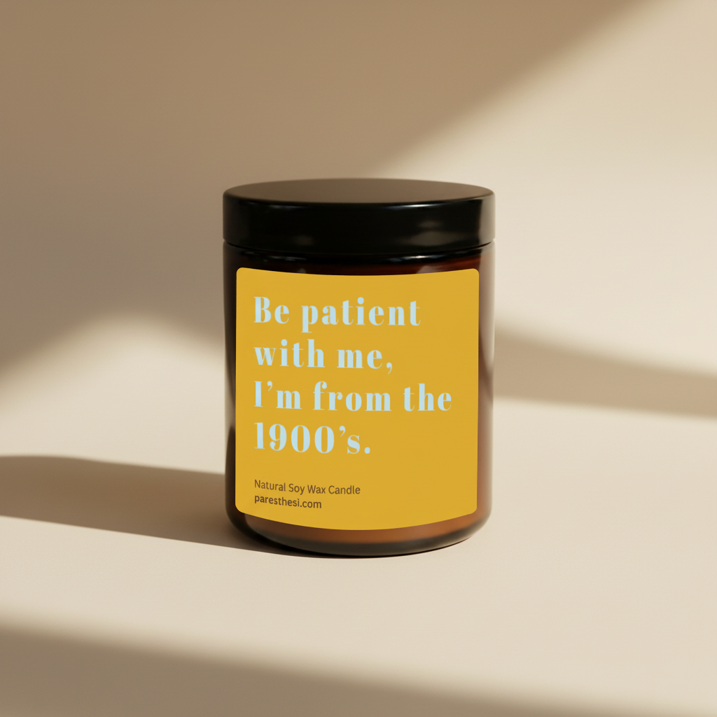 An amber glass jar candle with a black lid and a mustard yellow label featuring the text 'Be patient with me, I'm from the 1900's.' in light blue, on a plain beige background.