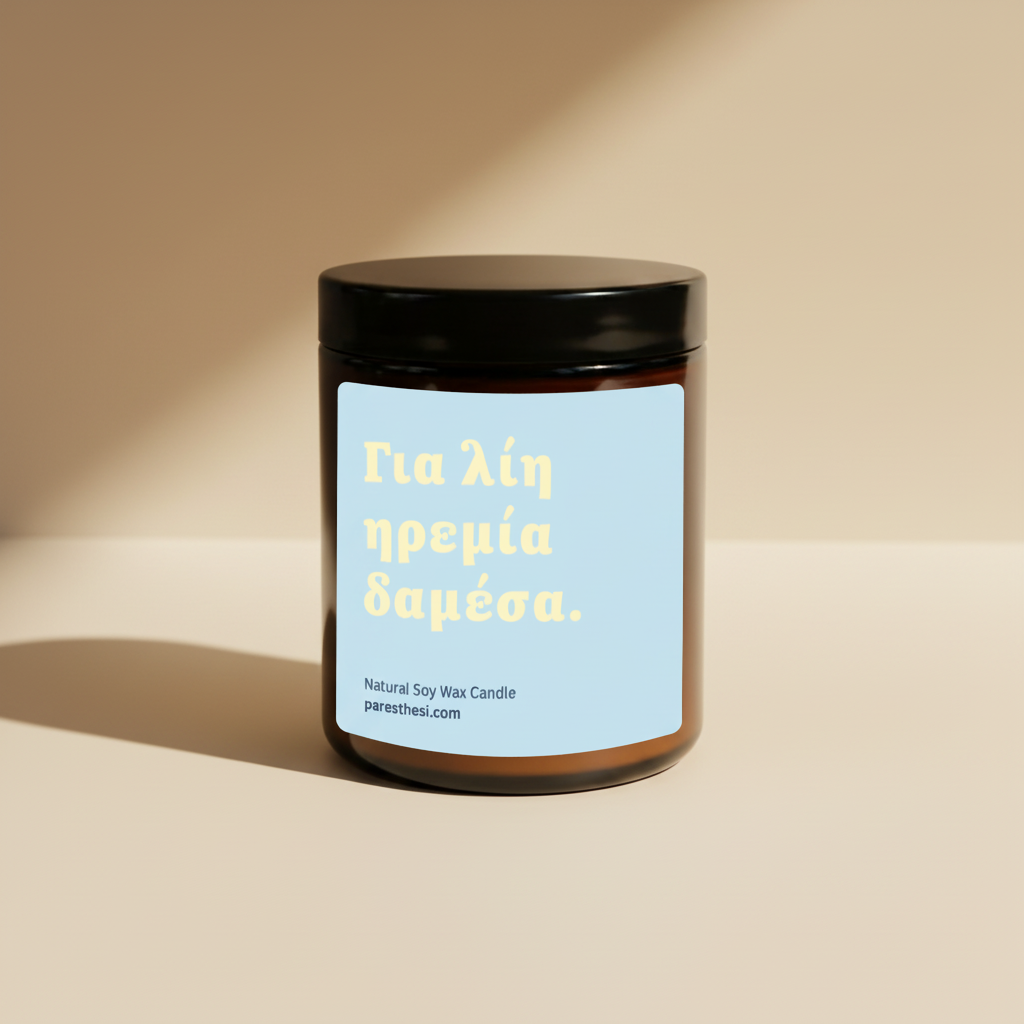 An amber glass jar candle with a black lid and a light blue label featuring yellow Greek text, set against a beige background.