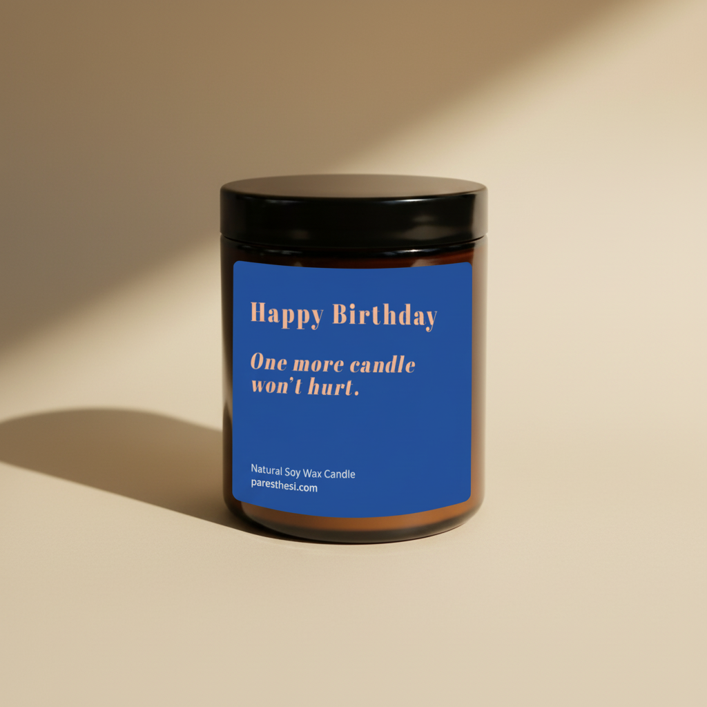 A dark amber glass jar candle with a black lid and a blue label that reads 'Happy Birthday. One more candle won't hurt.' in light orange color on a beige background.