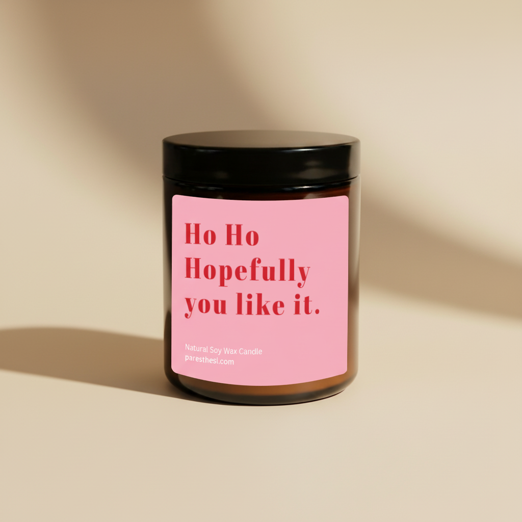 A natural soy wax candle in an amber glass jar with a black lid and a pink label that reads 'Ho Ho Hopefully you like it.' in red text, on a solid beige background.