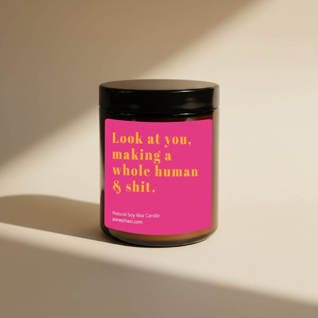 A jar candle with a black lid and a bright pink label featuring yellow text that reads, 'Look at you, making a whole human & shit.' Small text at the bottom reads 'Natural Soy Wax Candle' and 'paresthesi.com'.