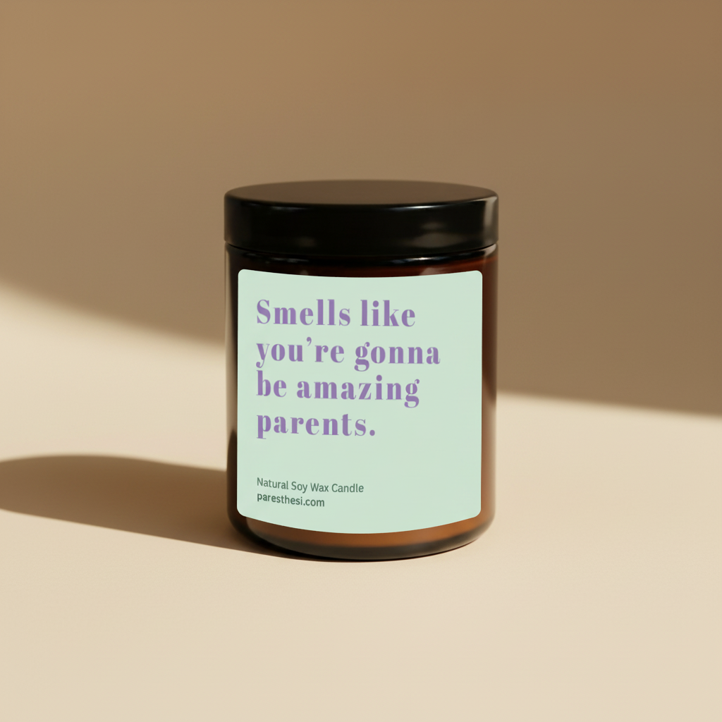 An amber glass jar candle with a black lid and a light mint-green label featuring purple text that reads, 'Smells like you're gonna be amazing parents.' The candle is photographed on a warm beige background with a soft shadow.