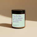 An amber glass jar candle with a black lid and a light mint-green label featuring purple text that reads, 'Smells like you're gonna be amazing parents.' The candle is photographed on a warm beige background with a soft shadow.
