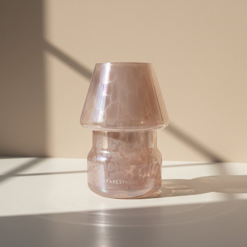 Iridescent  pink lamp with candle on a beige surface with soft shadows