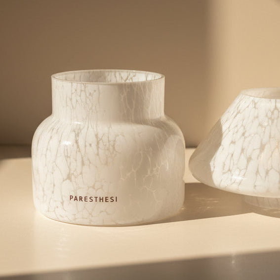 Candle in a patterned glass holder on a beige surface with a soft shadow