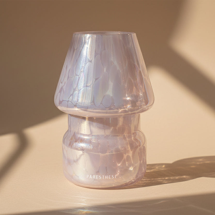 Iridescent glass vase with candle on a beige surface with soft shadows