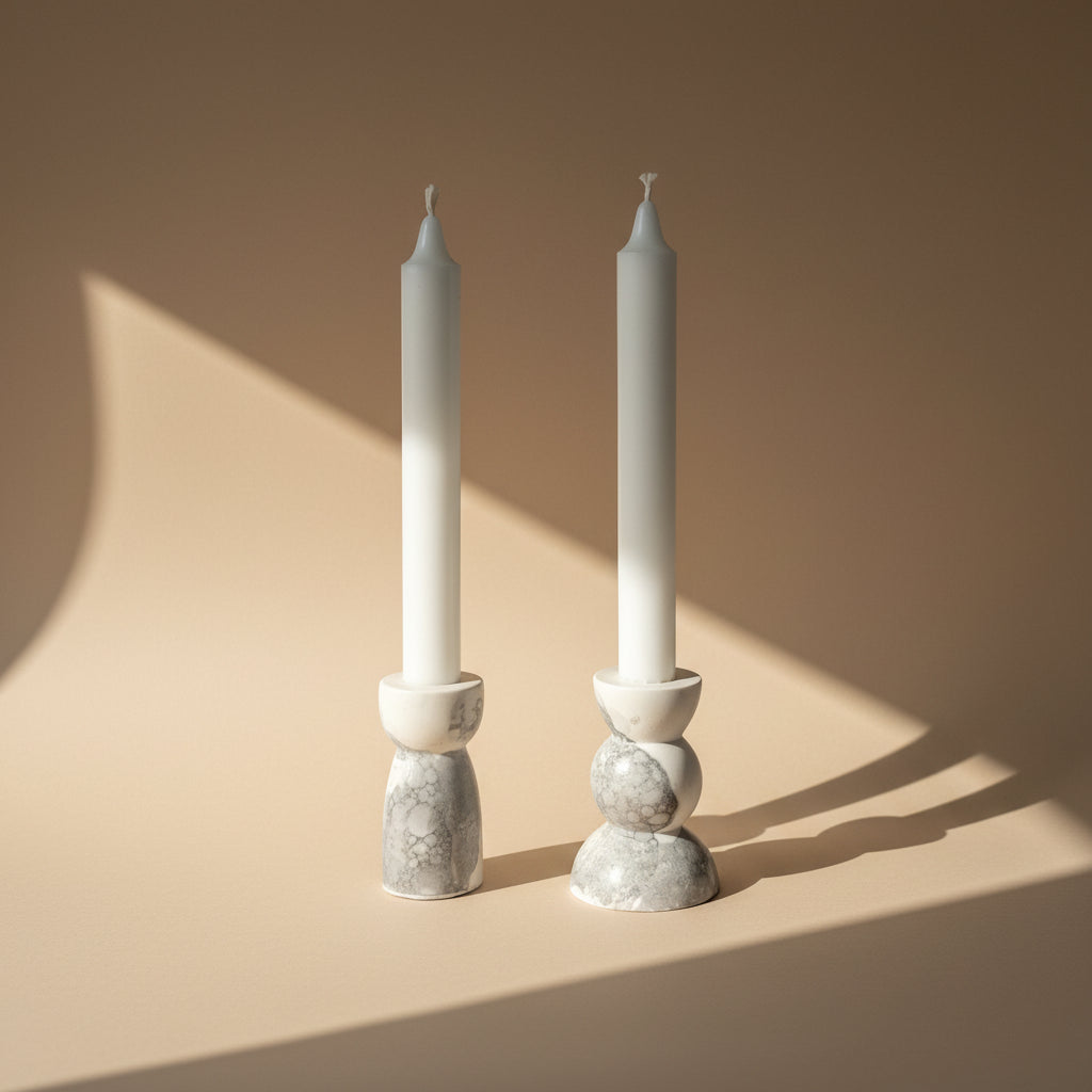 Two white candles in porcelain candle holders with a marble texture on a beige background