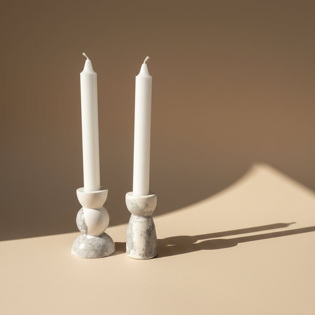 Two white candles in porcelain candle holders with a marble texture on a beige background
