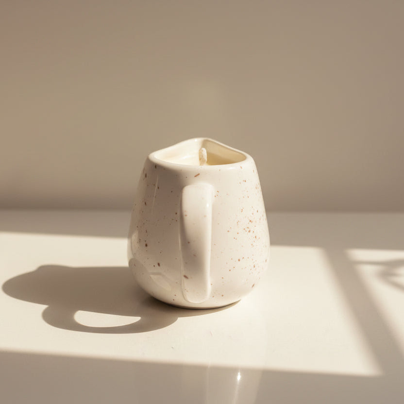 White porcelain vessel with a massage candle on a reflective surface with soft shadows