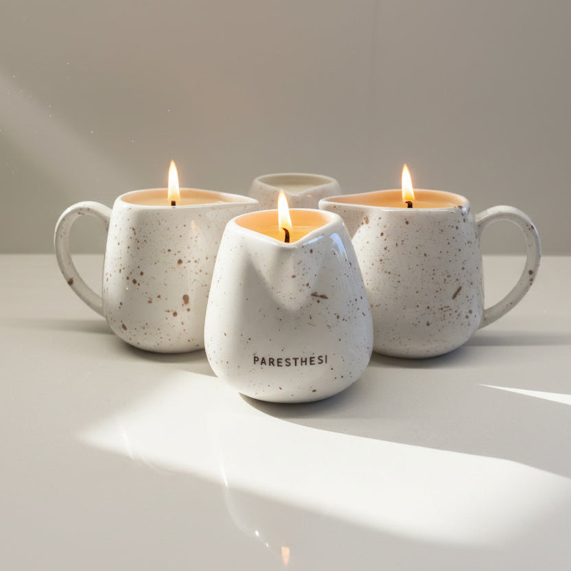 Four ceramic mugs with massage candles inside on a white surface.