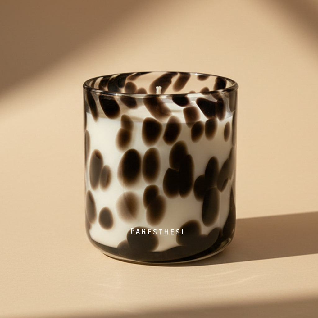 Candle in a glass holder with a leopard print pattern on a beige background, featuring the brand 'PARESTHESI'.
