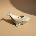 Whale-shaped porcelain vessel with a candle on a light beige surface