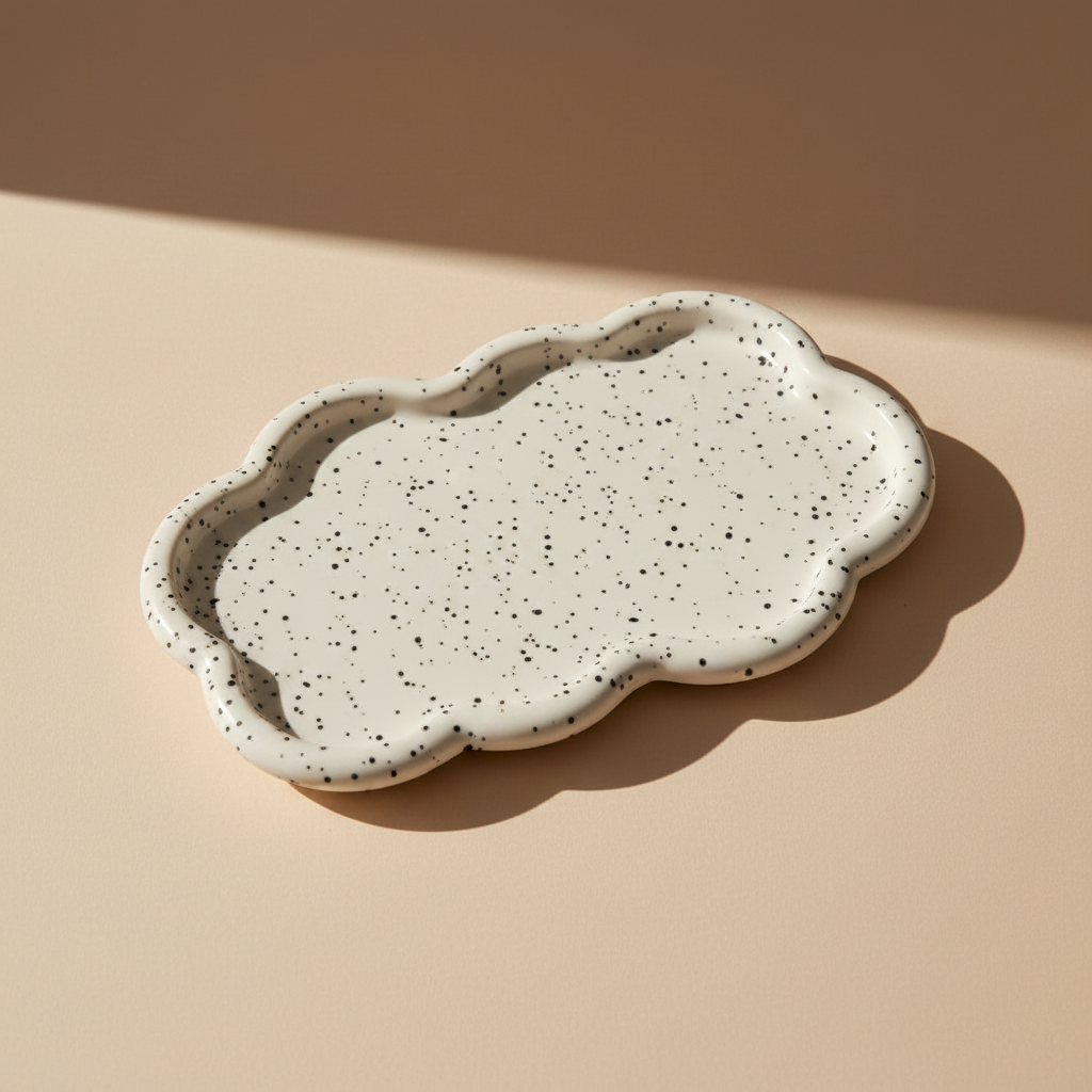 Speckled white and black porcelain cloud-shaped tray on a beige surface with a neutral background