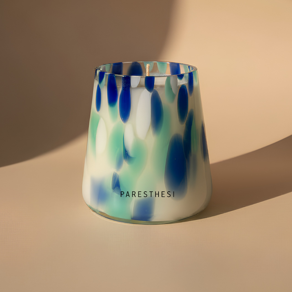 Glass candle holder with blue and green abstract pattern on a beige background
