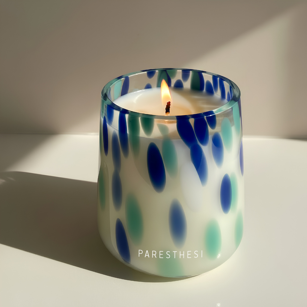 Glass candle holder with blue and green abstract pattern on a beige background