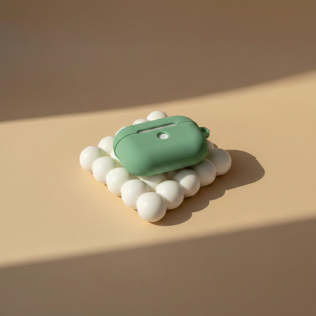 A mint green AirPods case resting on a cluster of white spherical props against a warm beige background with soft diagonal shadows.