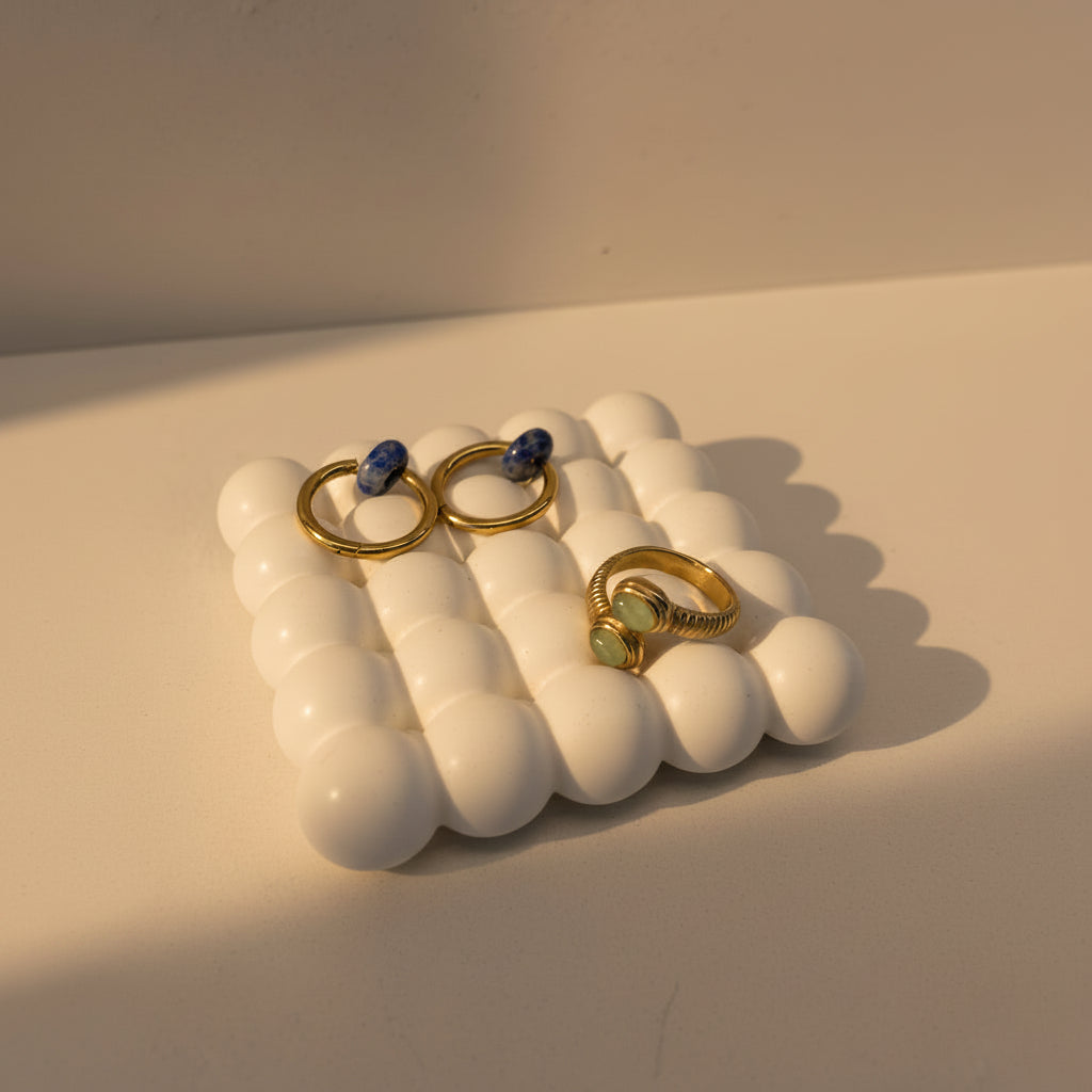 Ring and earrings displayed on a white bubbled tray against a warm beige background with soft shadows.