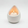 White porcelain teardrop-shaped candle holder with a lit candle inside on a light gray background
