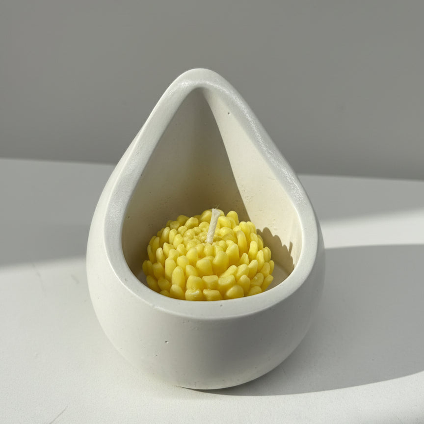 Teardrop-shaped white candle holder with a yellow chrysanthemum candle on a light gray background