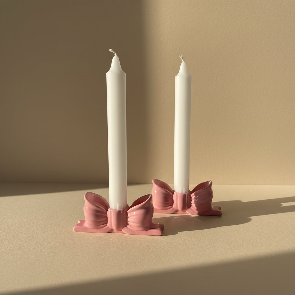 Two white candles in pink candle holders in a ribbon -shaped, on a beige background