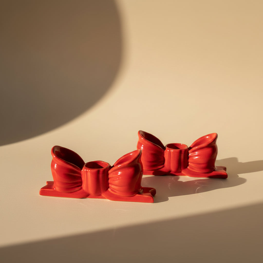 Two white candles in red candle holders in a ribbon - shaped, on a beige background