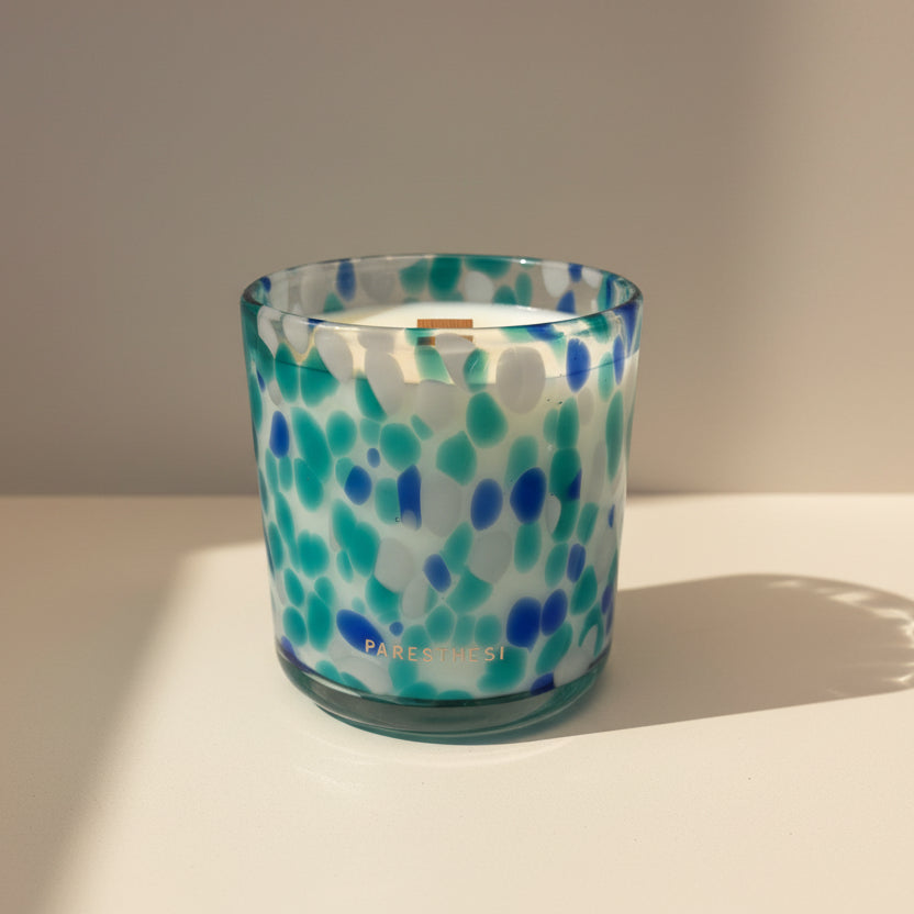 Candle in a glass jar with blue and green pattern on a white surface