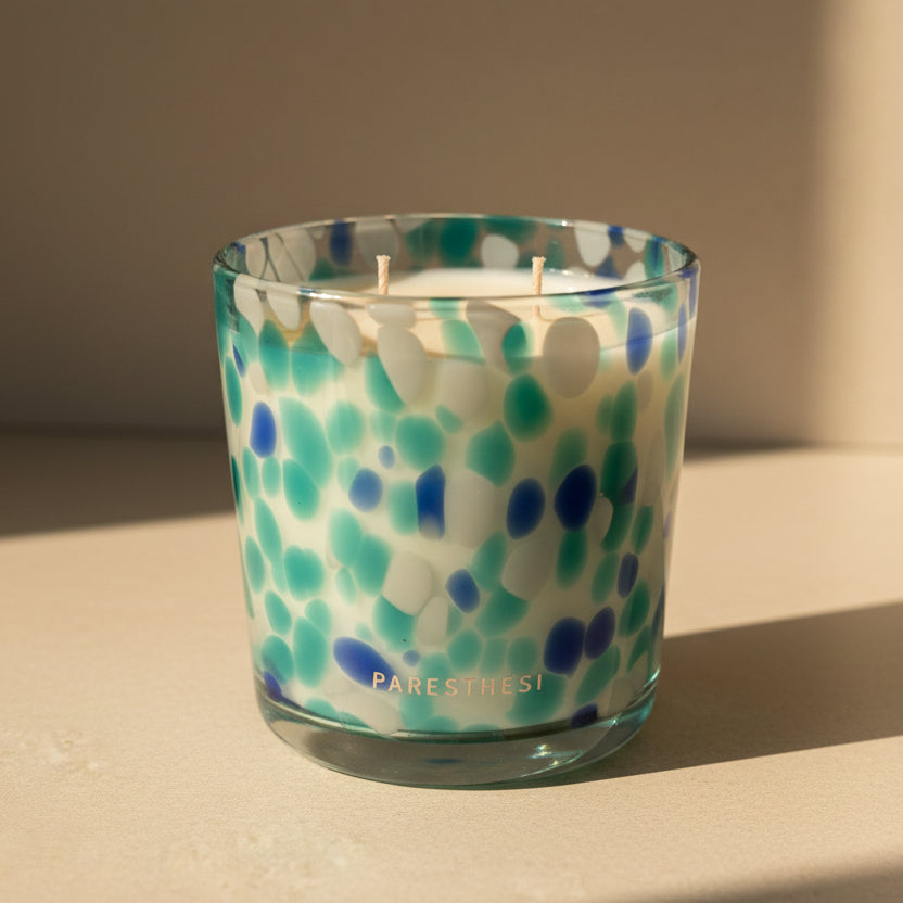 Candle in a glass jar and a pattern of blue and green dots on a beige surface.