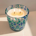 Candle in a glass container with blue and green pattern on a white surface