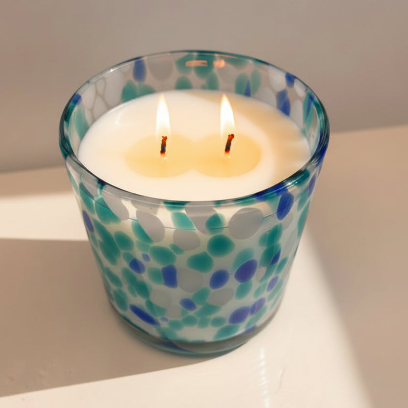 Candle in a glass container with blue and green pattern on a white surface