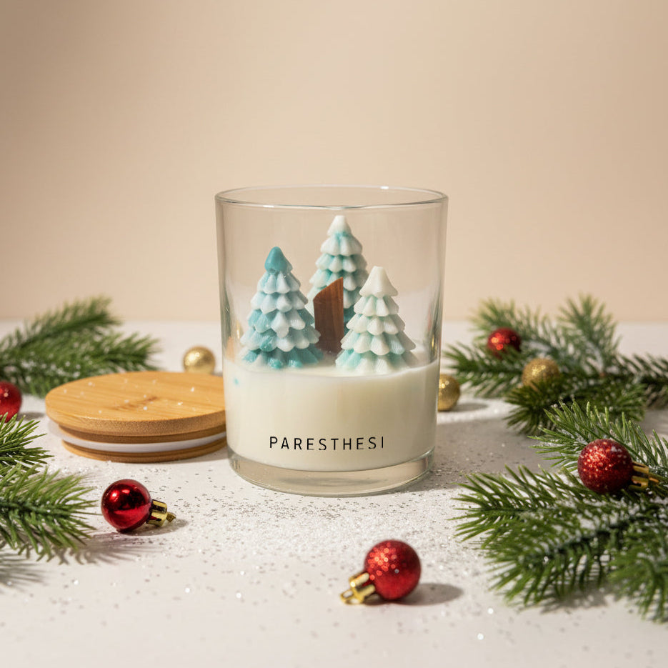 Candle with Christmas tree decorations and 'PARESTHESI' branding, surrounded by festive elements on a beige background.