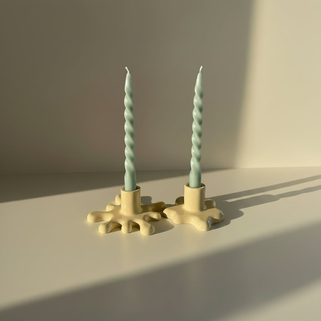 Two twisted candles in beige candle holders on a neutral background