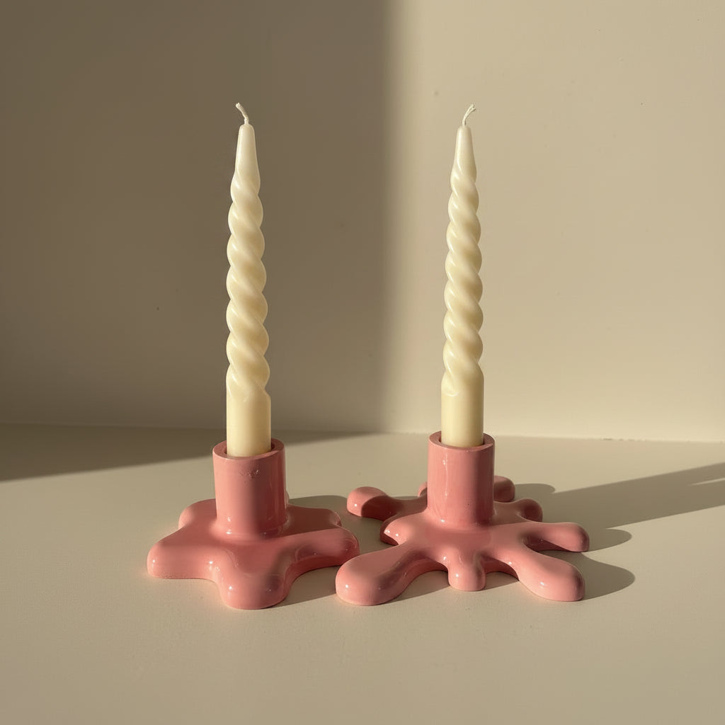 Two pink candle holders with twisted candles on a neutral background
